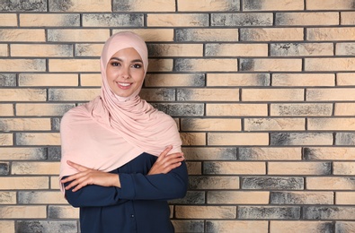 Portrait of young Muslim woman in hijab against brick wall. Space for text