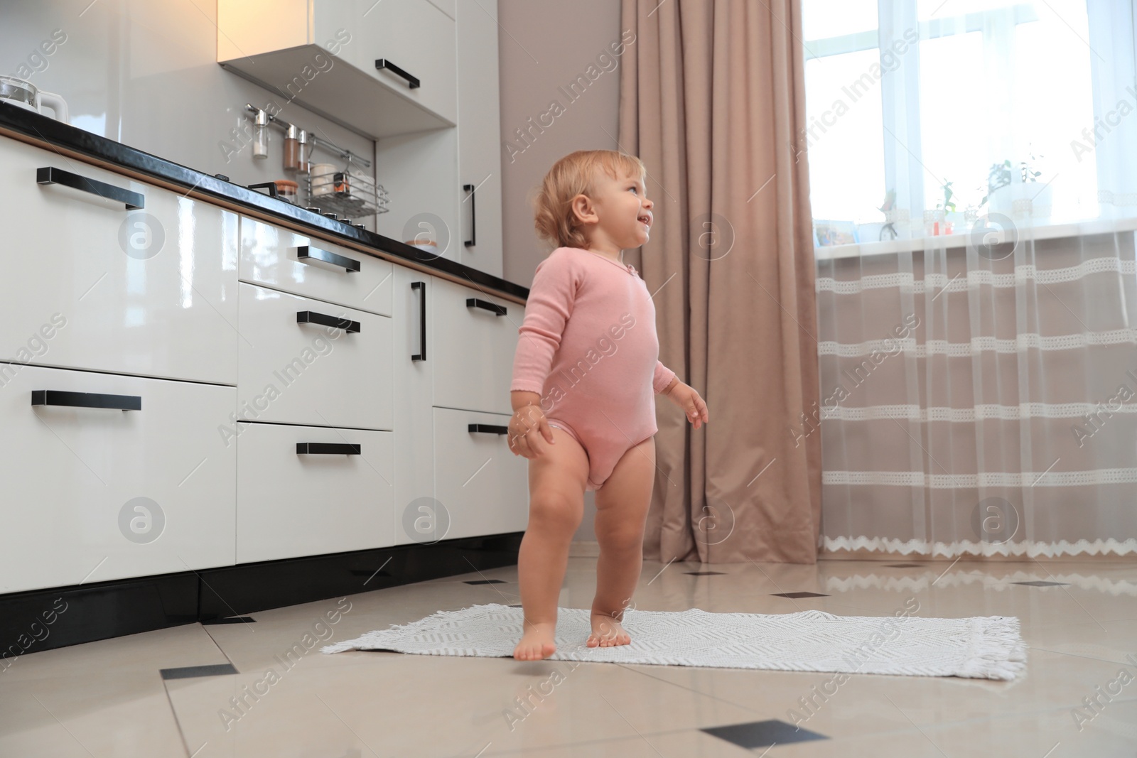 Photo of Cute baby learning to walk in kitchen near window