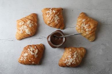 Photo of Delicious croissants with almond flakes and chocolate paste on grey table, flat lay