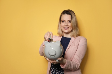 Photo of Beautiful businesswoman putting money into piggy bank on color background. Space for text