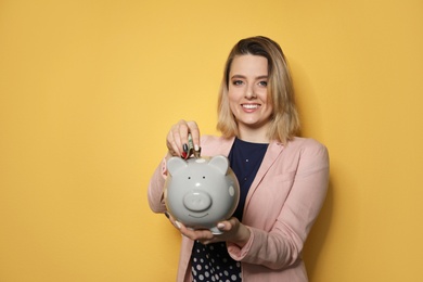 Beautiful businesswoman putting money into piggy bank on color background. Space for text