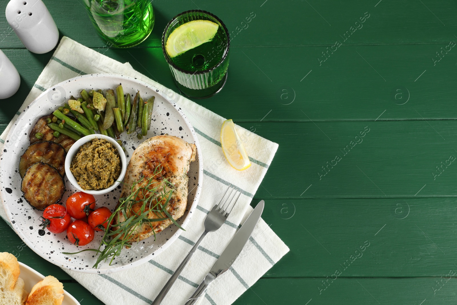 Photo of Tasty chicken, vegetables, drink with tarragon and pesto sauce served on green wooden table, flat lay. Space for text