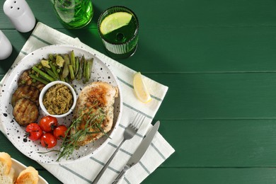 Photo of Tasty chicken, vegetables, drink with tarragon and pesto sauce served on green wooden table, flat lay. Space for text