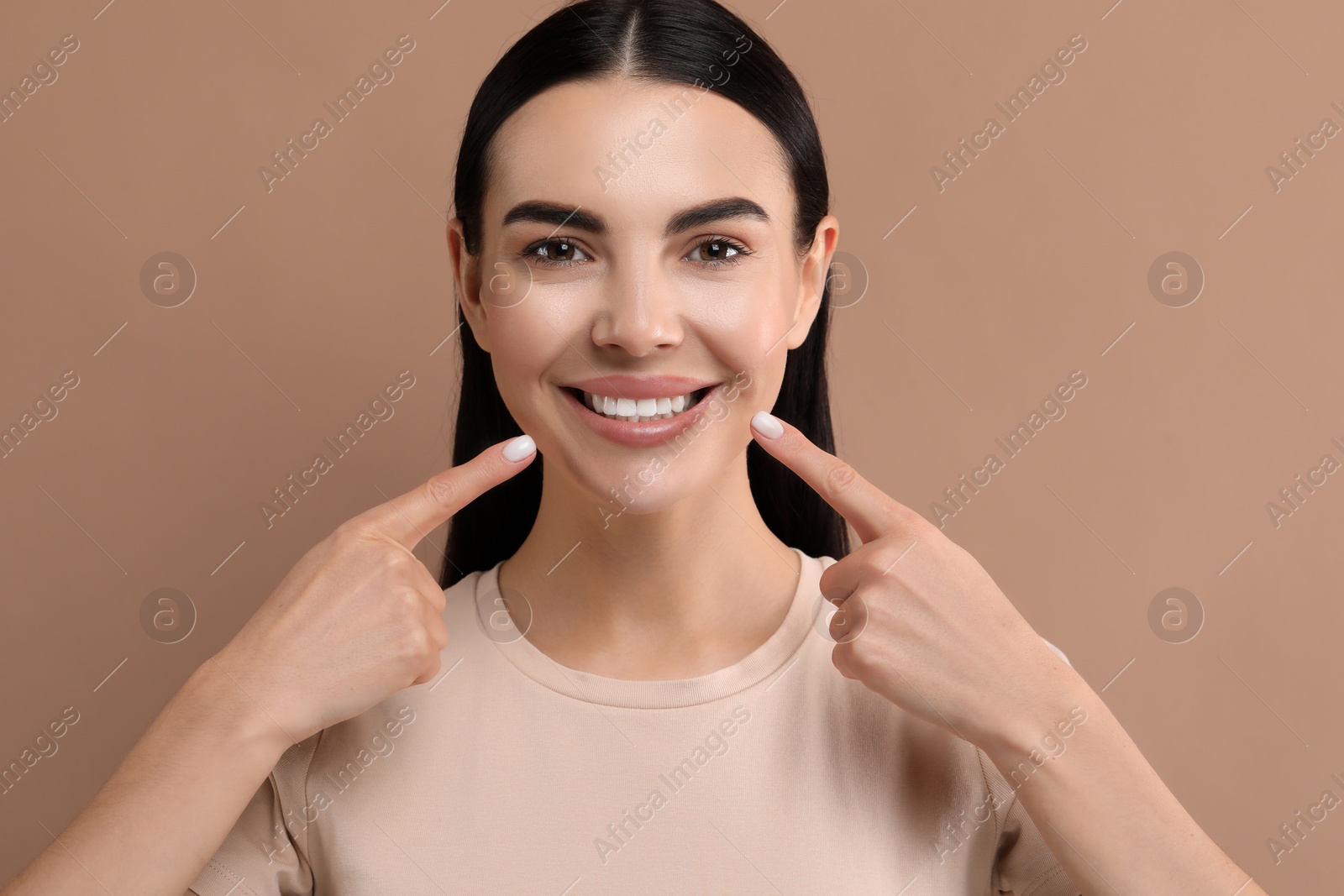 Photo of Beautiful woman showing her clean teeth and smiling on beige background