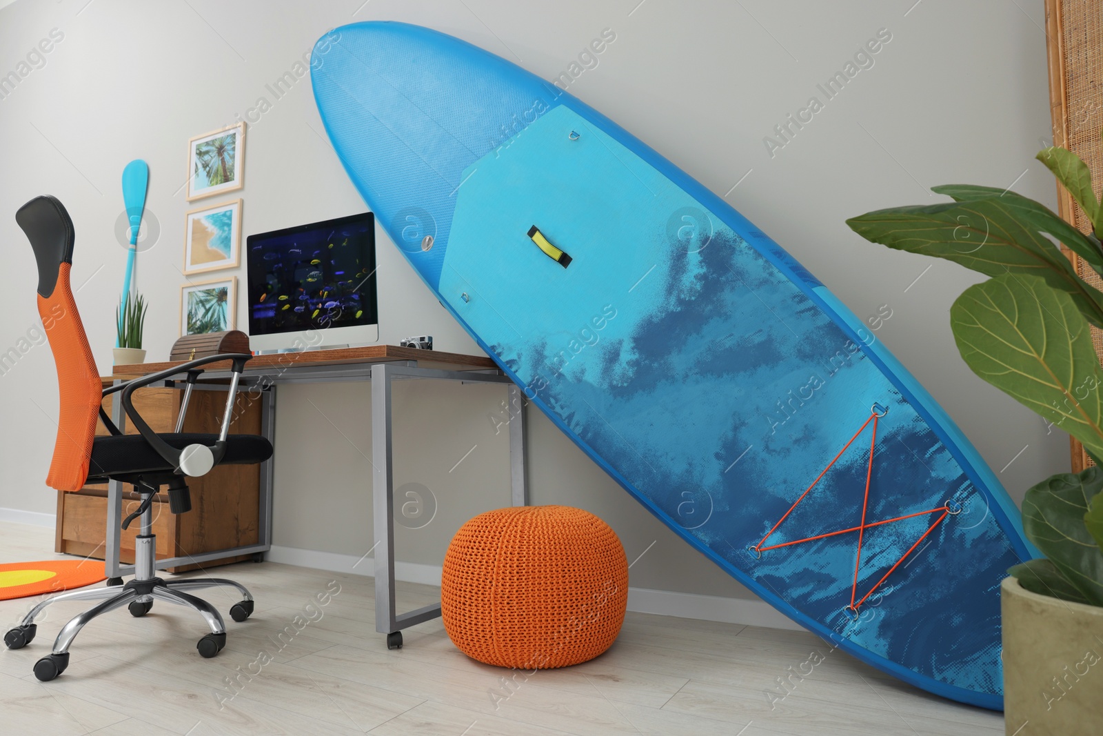 Photo of Stylish workplace with modern computer, SUP board and pouf at home. Interior design