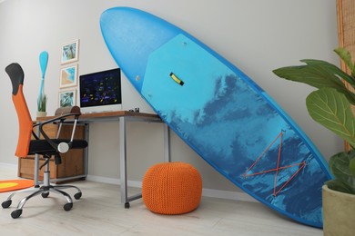 Stylish workplace with modern computer, SUP board and pouf at home. Interior design