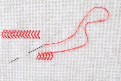 Photo of Canvas with red embroidery and needle, top view