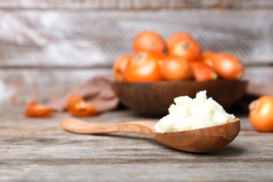 Photo of Spoon with fresh chopped onion on wooden table