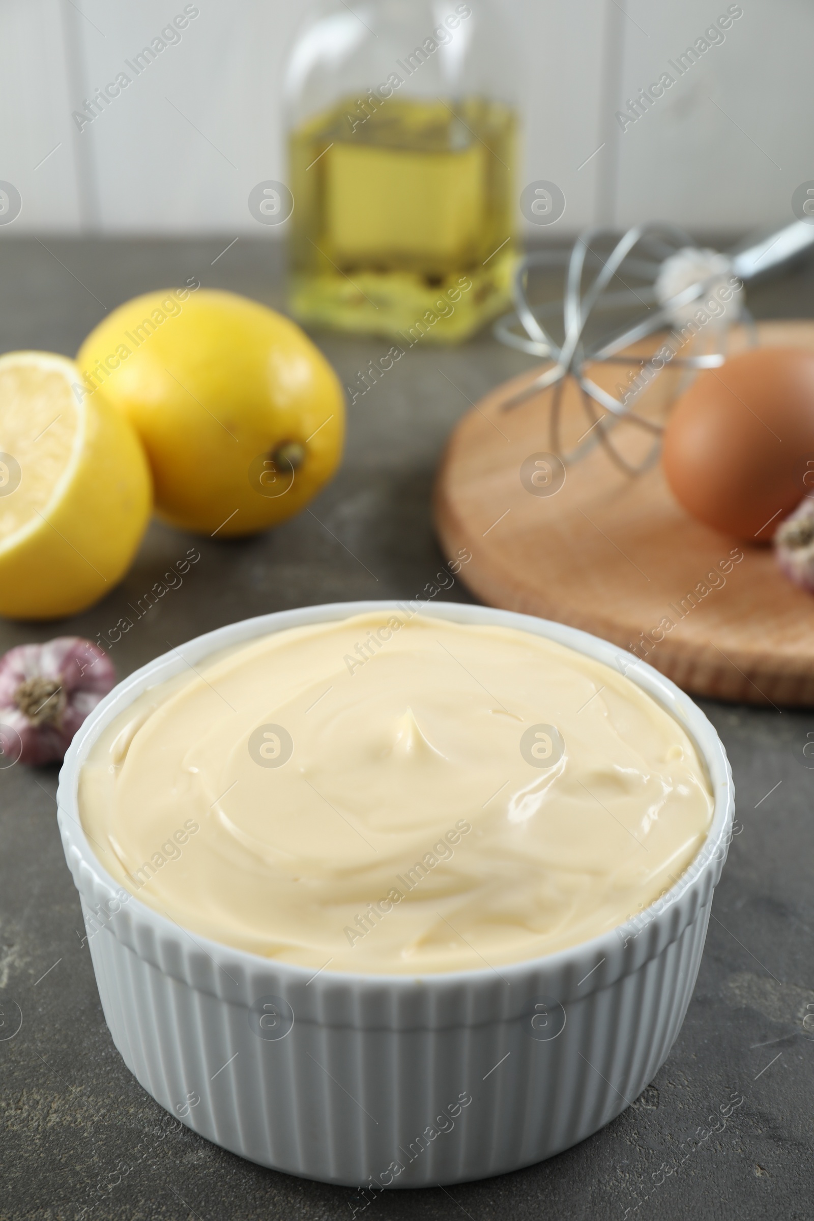 Photo of Fresh mayonnaise sauce in bowl and ingredients on grey table