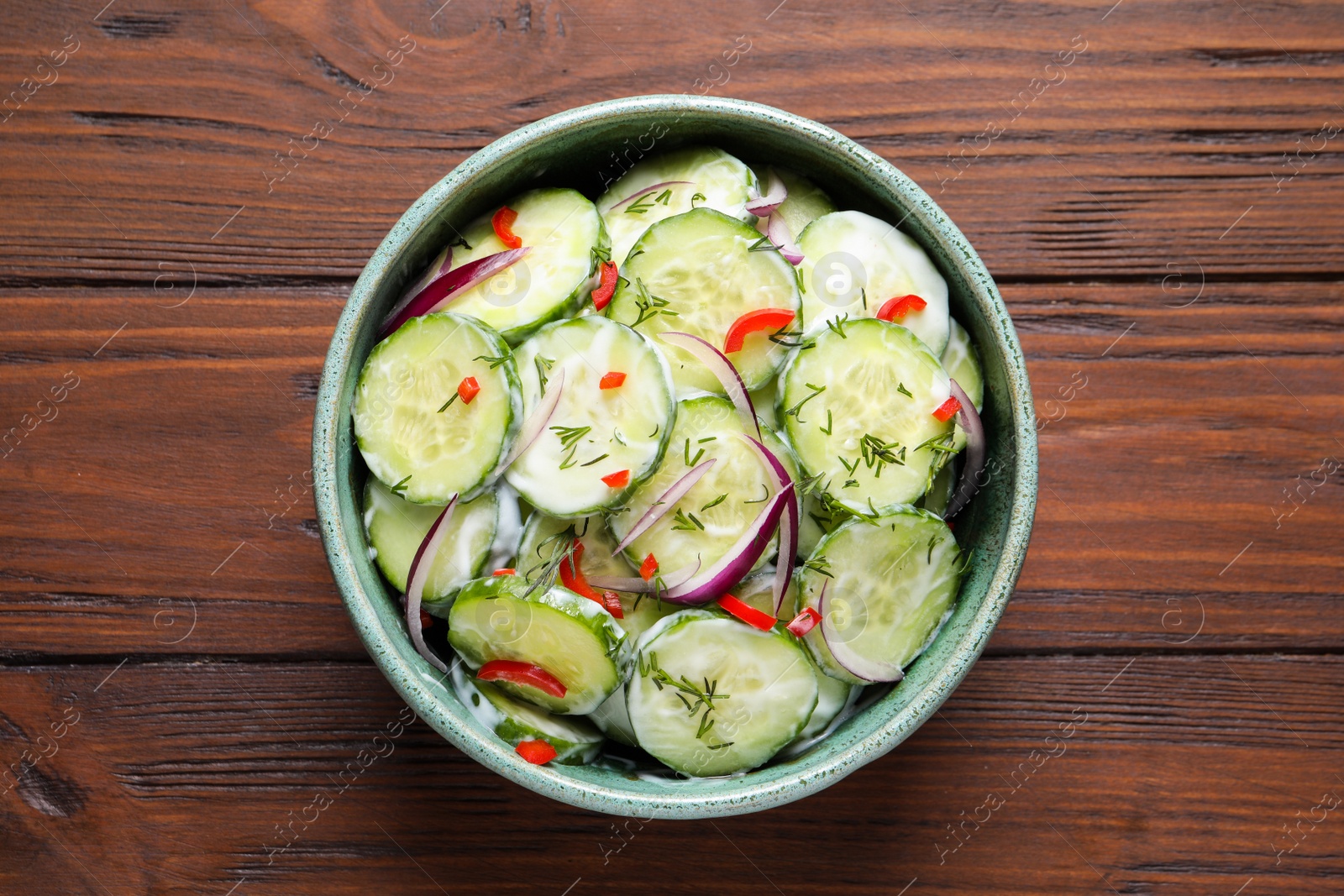 Photo of Dish with fresh creamy cucumber salad on wooden table, top view