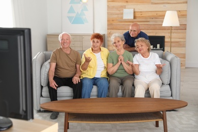 Happy elderly people watching TV together in living room