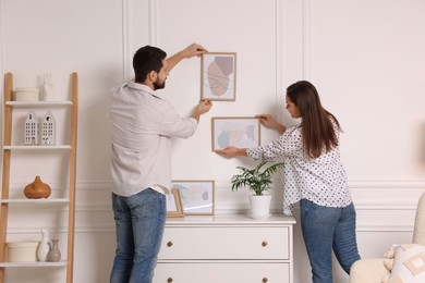 Photo of Man and woman hanging picture frames on white wall at home