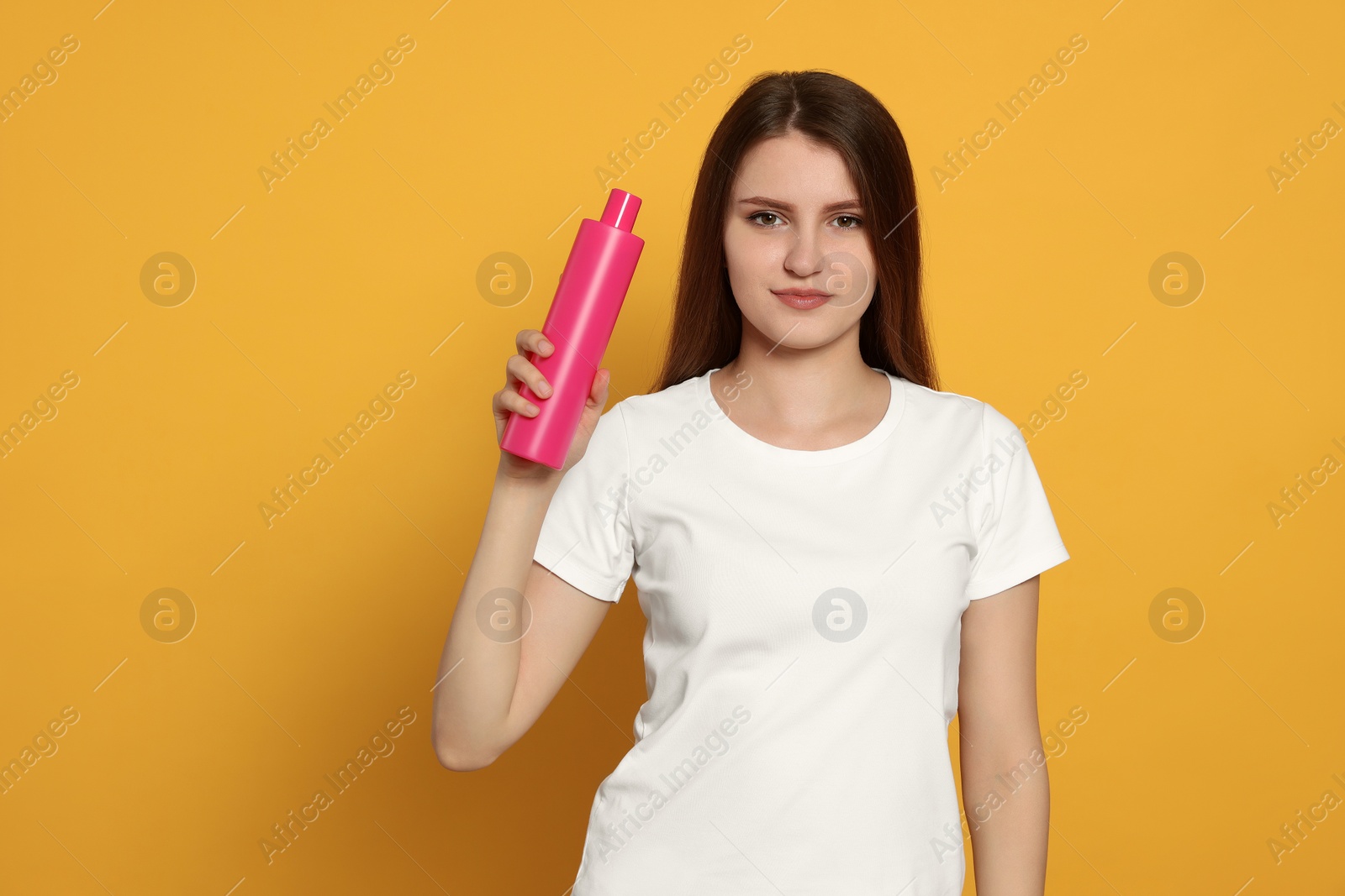 Photo of Beautiful young woman holding bottle of shampoo on yellow background