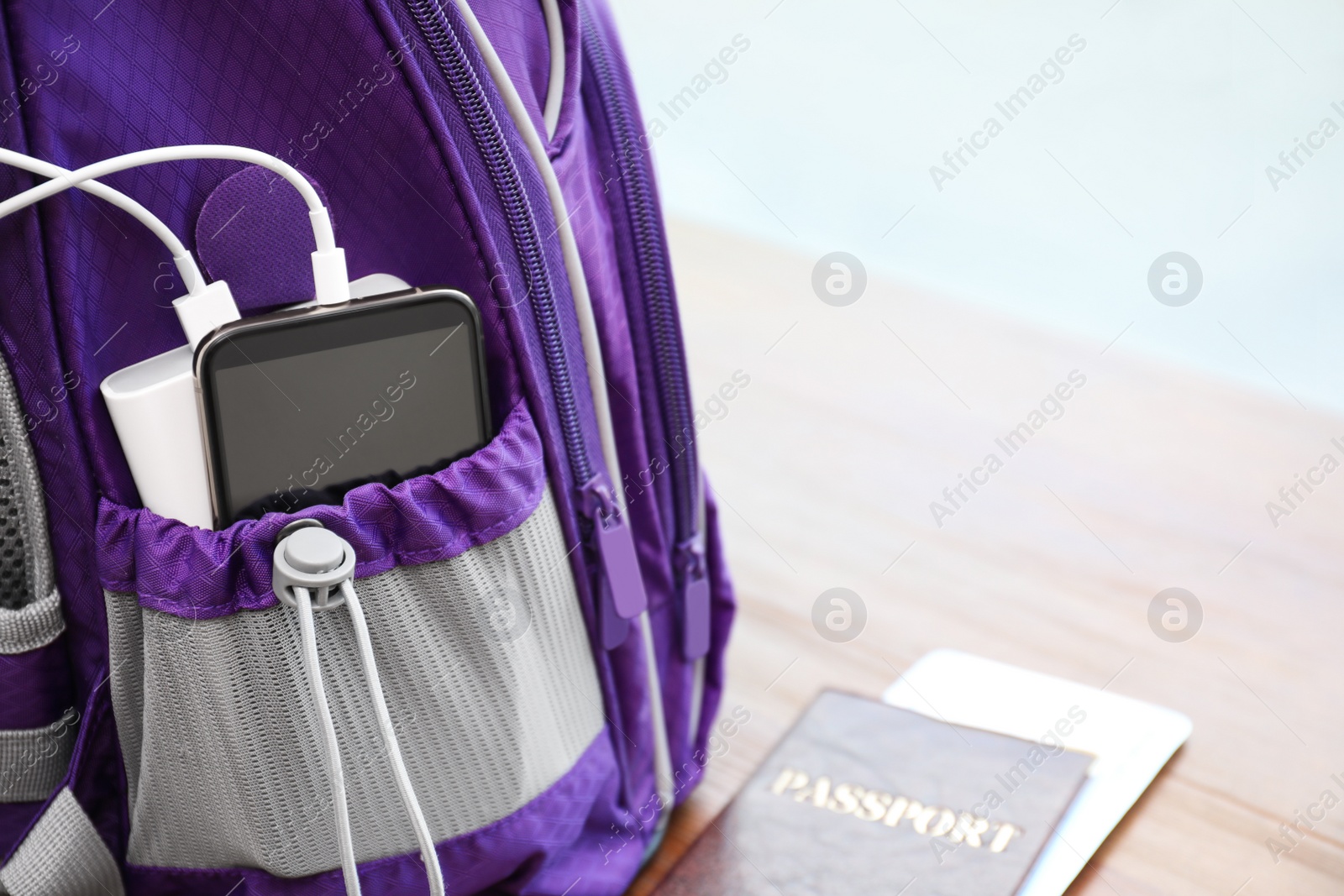 Photo of Charging mobile phone with power bank in purple backpack and passport on table, closeup. Space for text