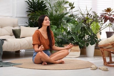 Beautiful woman meditating in living room decorated with houseplants. Interior design