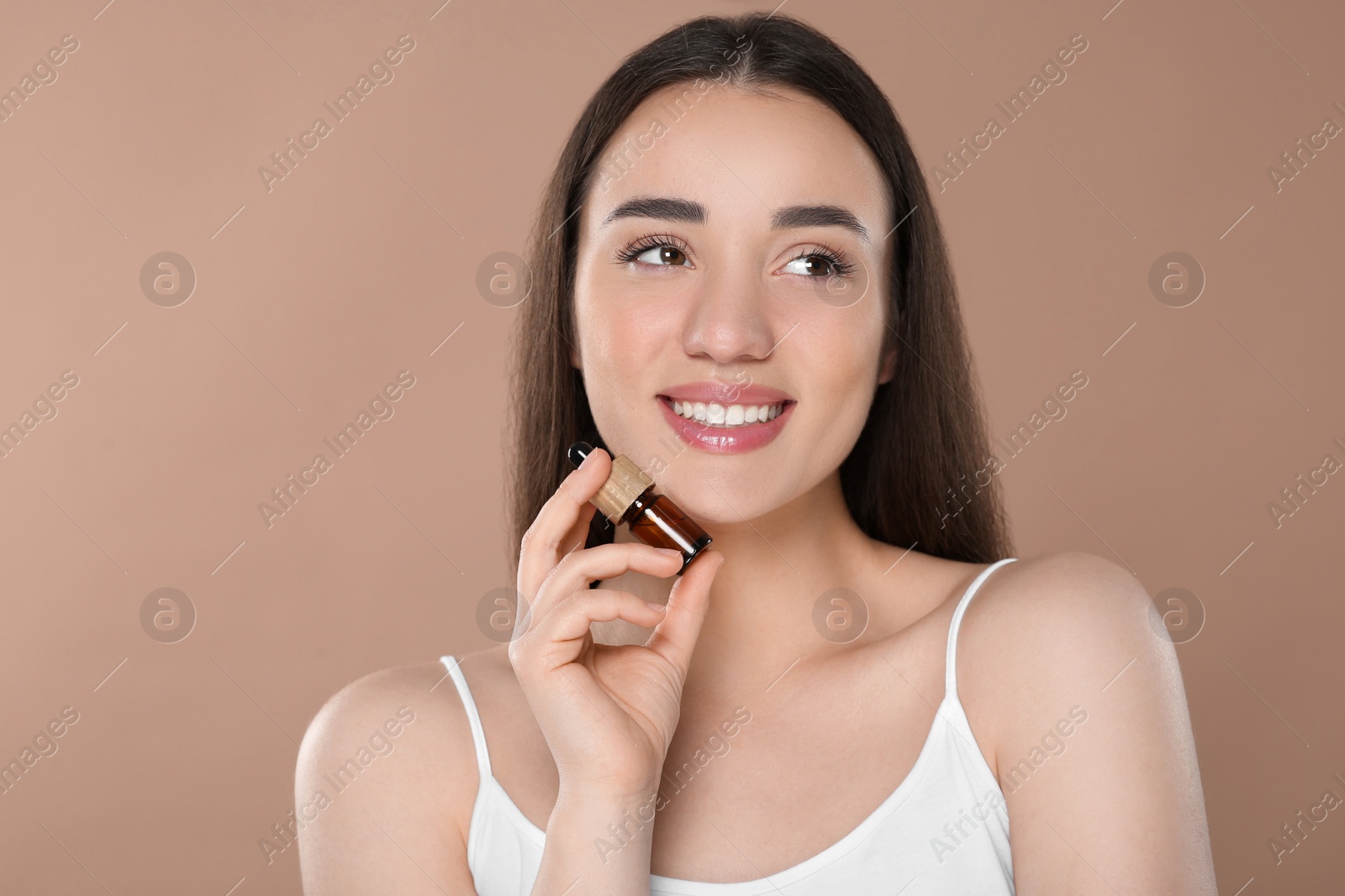 Photo of Beautiful young woman with bottle of essential oil on brown background