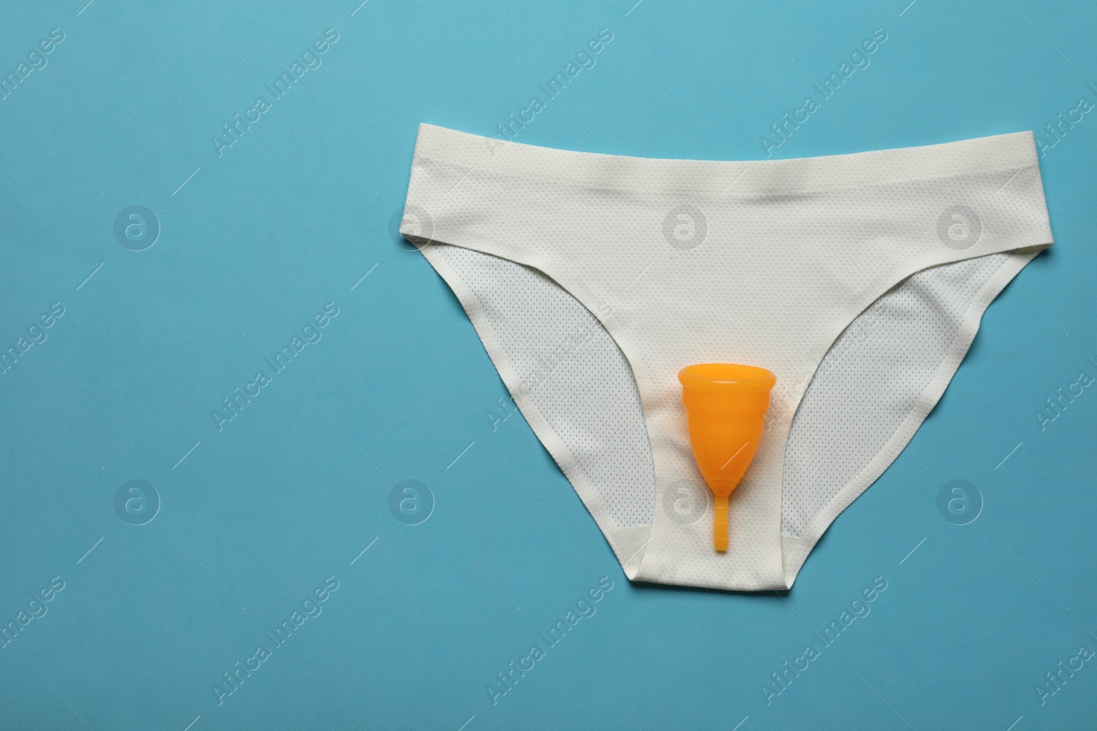 Photo of Menstrual cup and white underwear on light blue background, top view with space for text. Reusable female hygiene product
