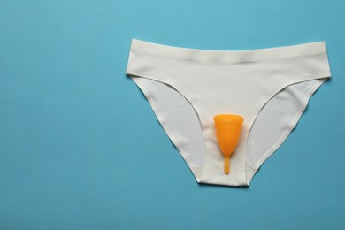 Menstrual cup and white underwear on light blue background, top view with space for text. Reusable female hygiene product