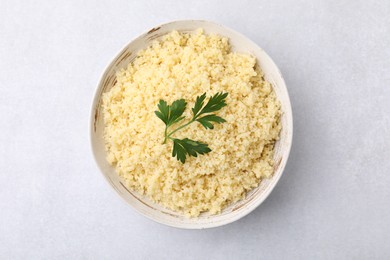 Photo of Tasty couscous and fresh parsley in bowl on light grey table, top view