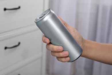 Photo of Woman holding aluminum can with beverage on blurred background, closeup. Space for design