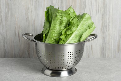 Photo of Colander with fresh green romaine lettuces on light grey table