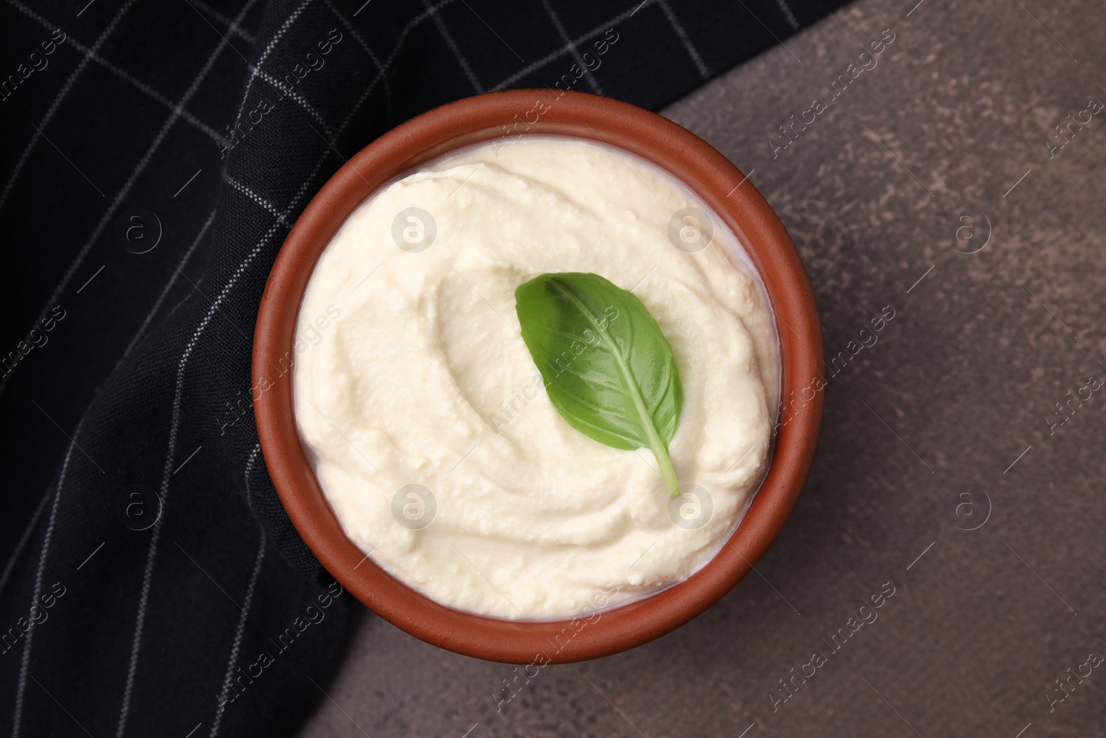 Photo of Delicious tofu sauce and basil leaf in bowl on brown table, top view