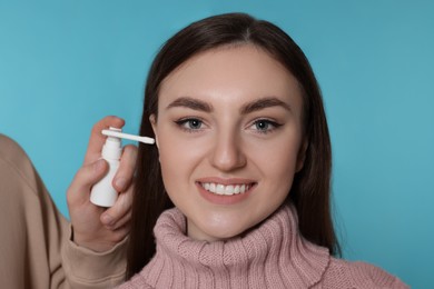 Man spraying medication into woman`s ear on light blue background