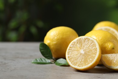 Fresh lemons and green leaves on grey table outdoors, closeup. Space for text