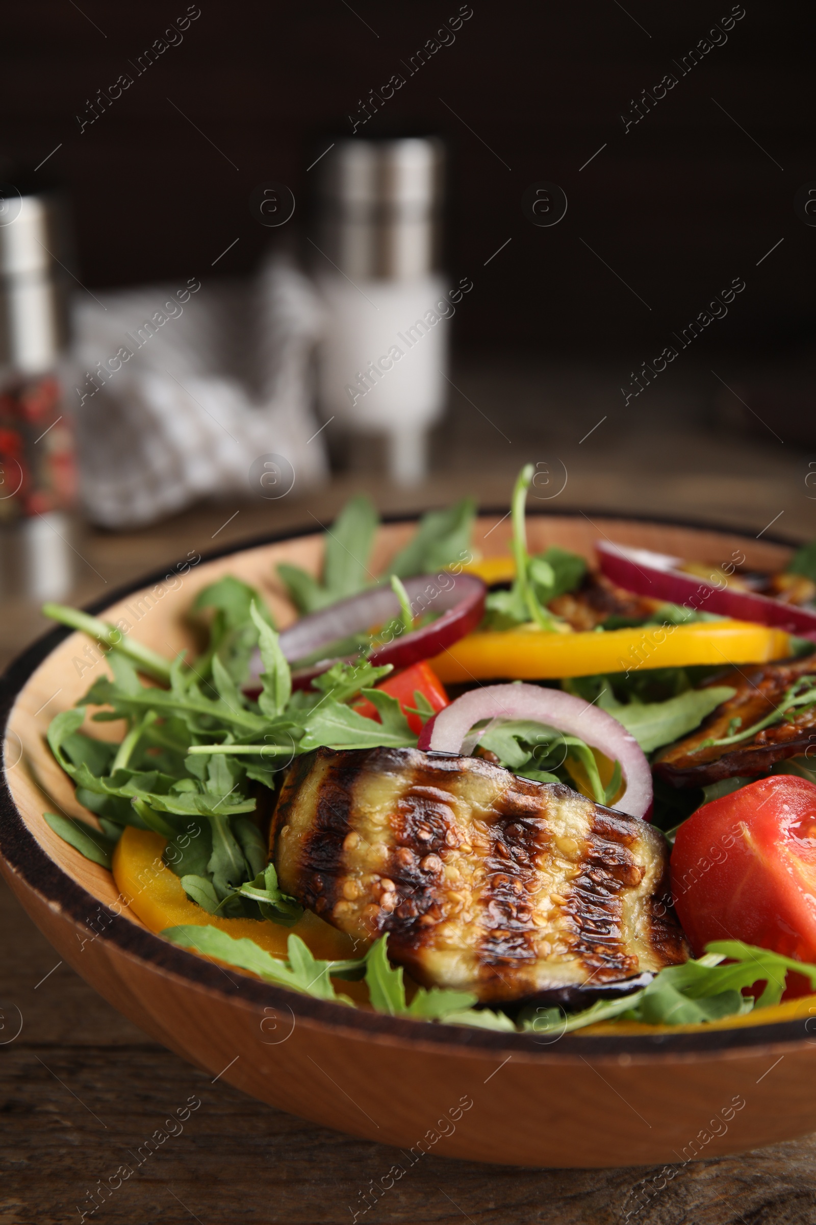 Photo of Delicious salad with roasted eggplant and arugula served on wooden table, closeup