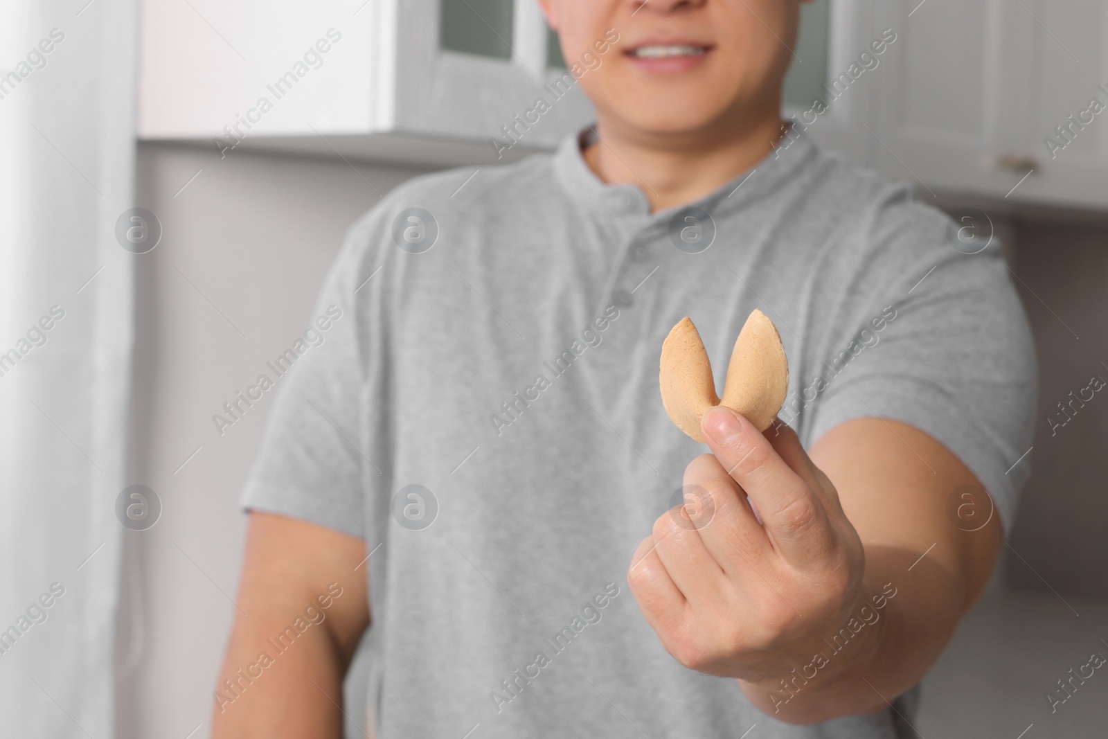 Photo of Man holding tasty fortune cookie with prediction indoors, closeup