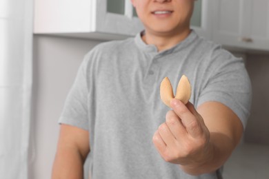 Man holding tasty fortune cookie with prediction indoors, closeup