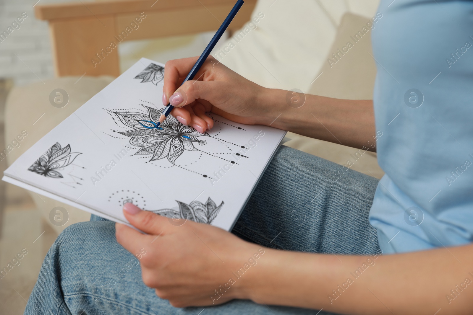 Photo of Young woman coloring antistress page on sofa, closeup
