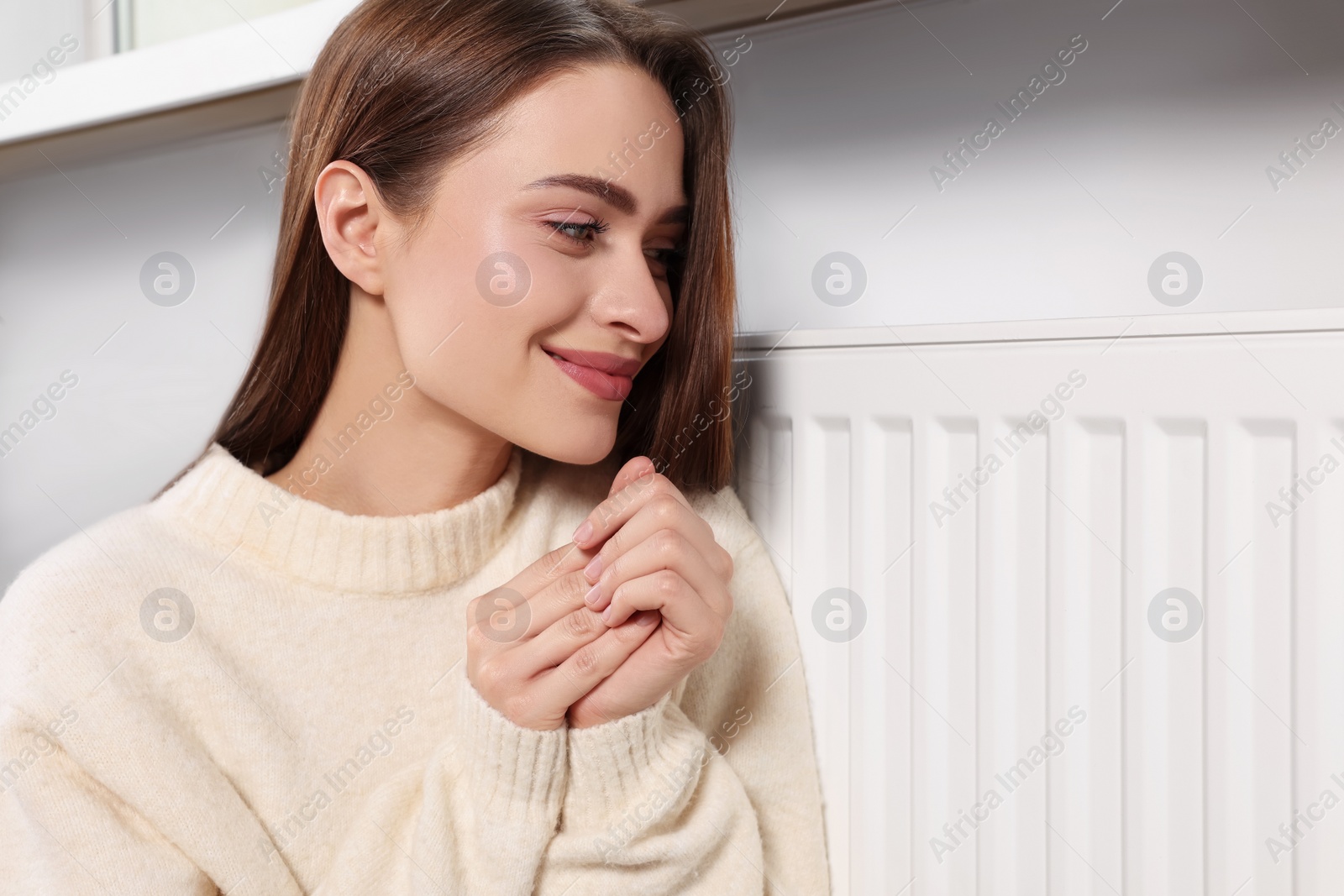 Photo of Woman warming hands on heating radiator indoors