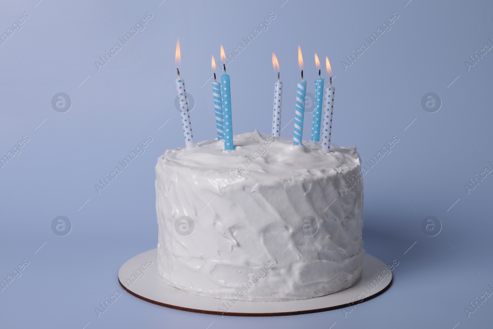 Photo of Delicious cake with cream and burning candles on light blue background