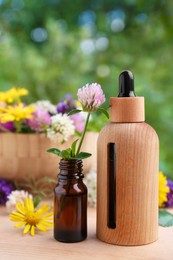 Photo of Bottles of essential oil and flowers on wooden table, closeup