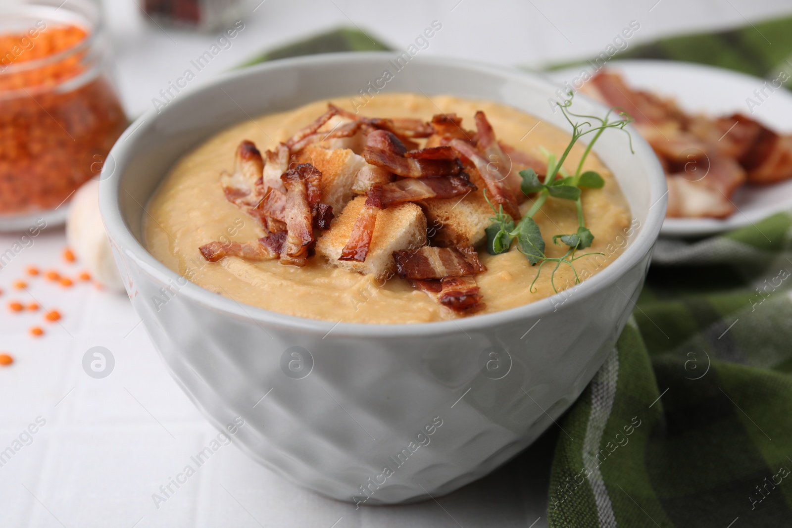 Photo of Delicious lentil soup with bacon and croutons on white table, closeup