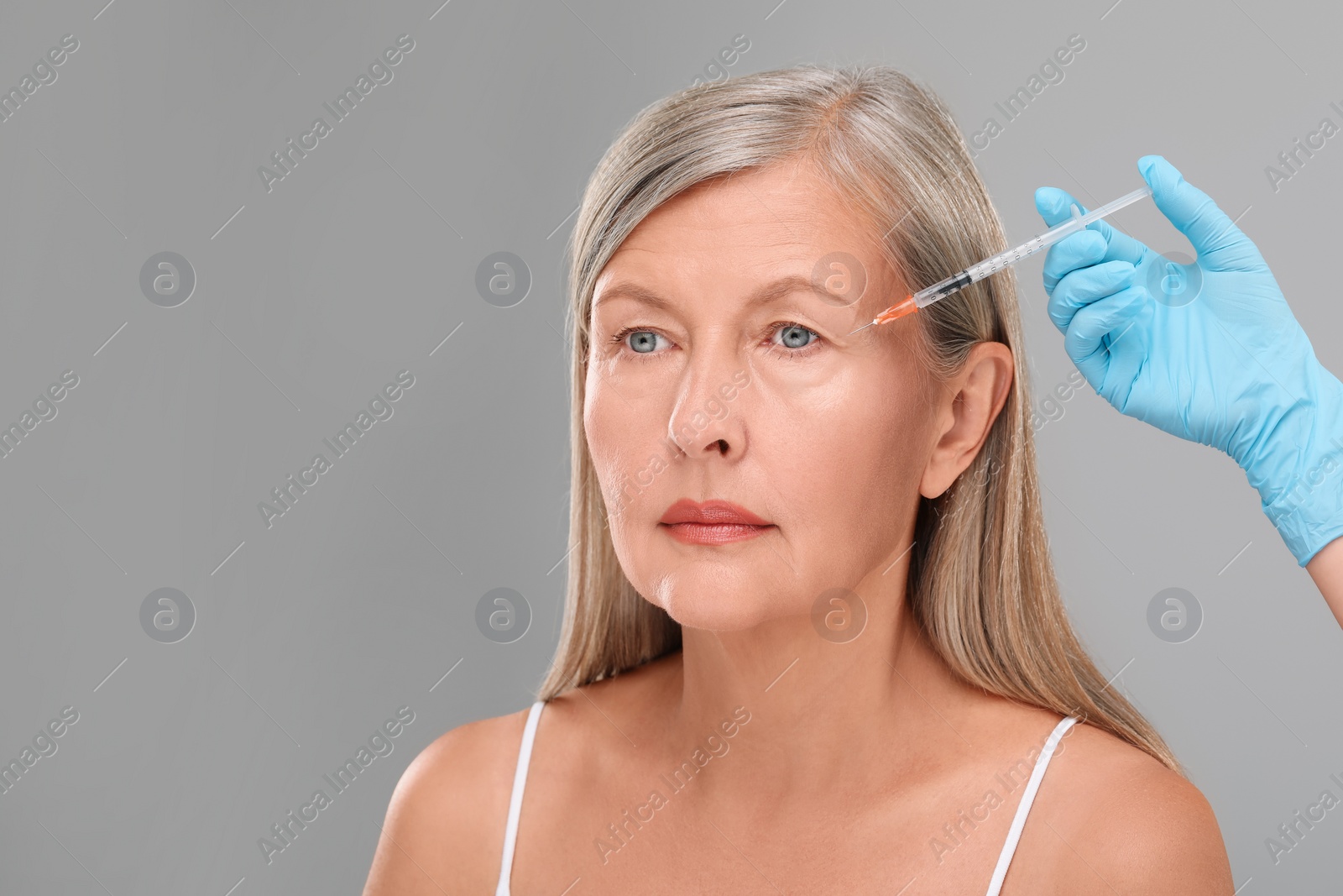 Photo of Doctor giving facial injection to senior woman on light grey background, closeup and space for text. Cosmetic surgery