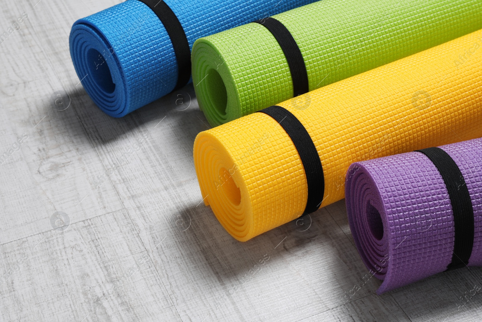 Photo of Bright rolled camping mats on white wooden background, closeup