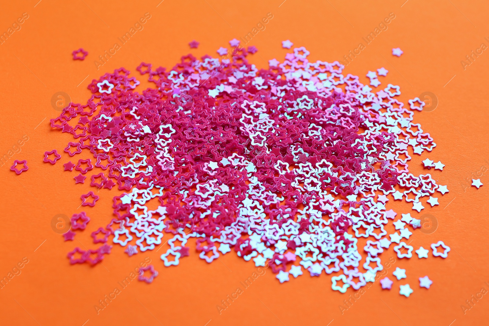 Photo of Shiny bright star shaped glitter on orange background