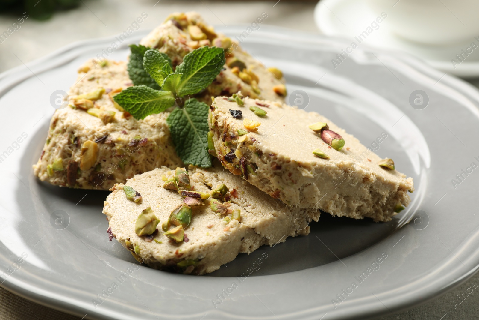 Photo of Tasty halva with pistachios and mint on table, closeup