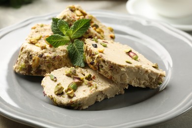 Photo of Tasty halva with pistachios and mint on table, closeup