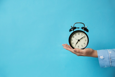 Photo of Closeup view of woman holding alarm clock on light blue background, space for text. Morning time