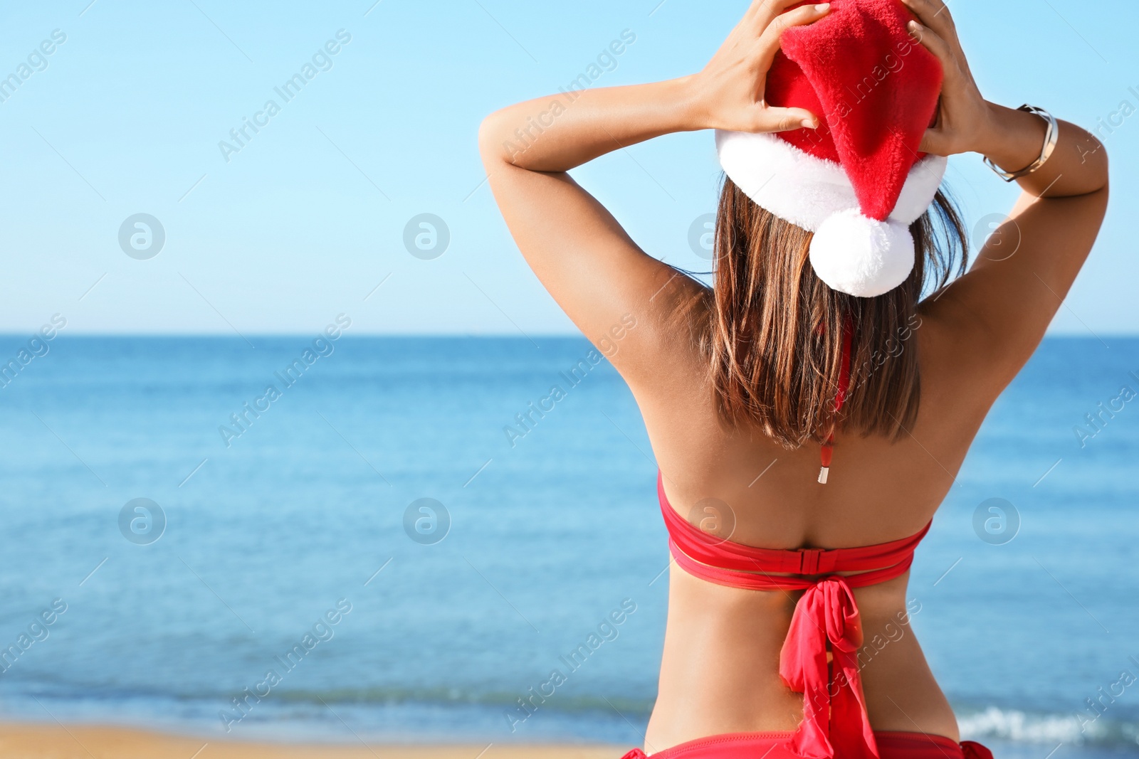 Photo of Young woman wearing Santa hat and bikini on beach, space for text. Christmas vacation