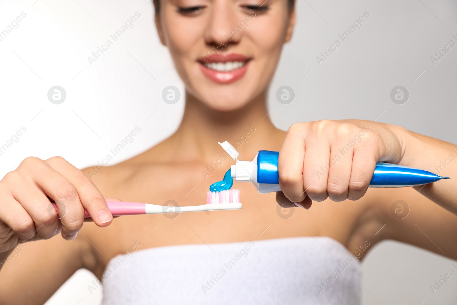 Photo of Woman applying toothpaste on brush against light background, closeup