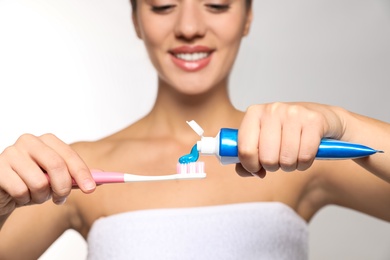 Woman applying toothpaste on brush against light background, closeup