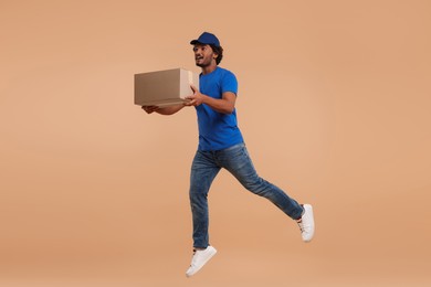 Photo of Happy courier with parcel jumping on light brown background