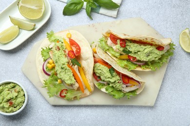 Photo of Delicious tacos with guacamole, meat and vegetables on light grey table, flat lay