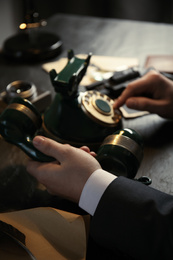 Photo of Detective dialing number on vintage telephone at table, closeup