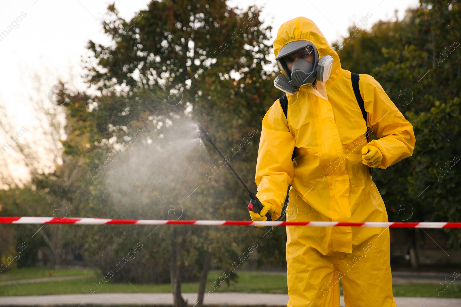 Photo of Person in hazmat suit disinfecting street with sprayer. Surface treatment during coronavirus pandemic