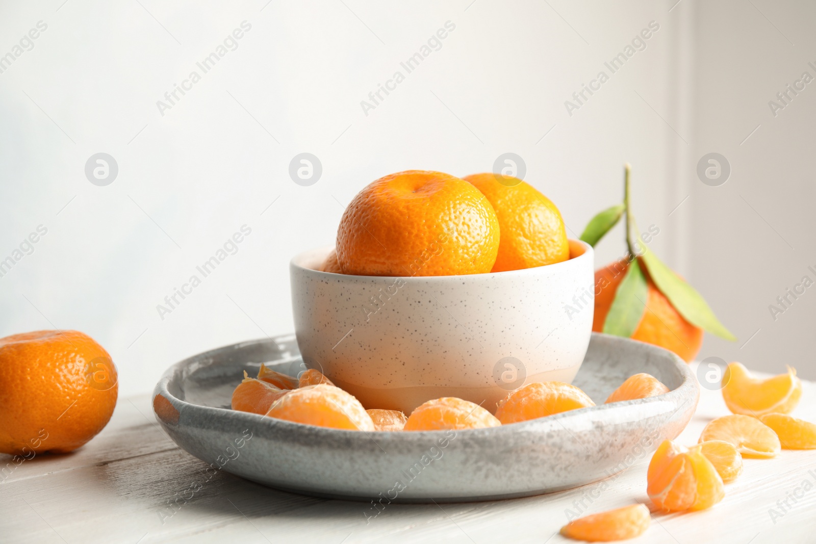 Photo of Plate and bowl with ripe tangerines on table